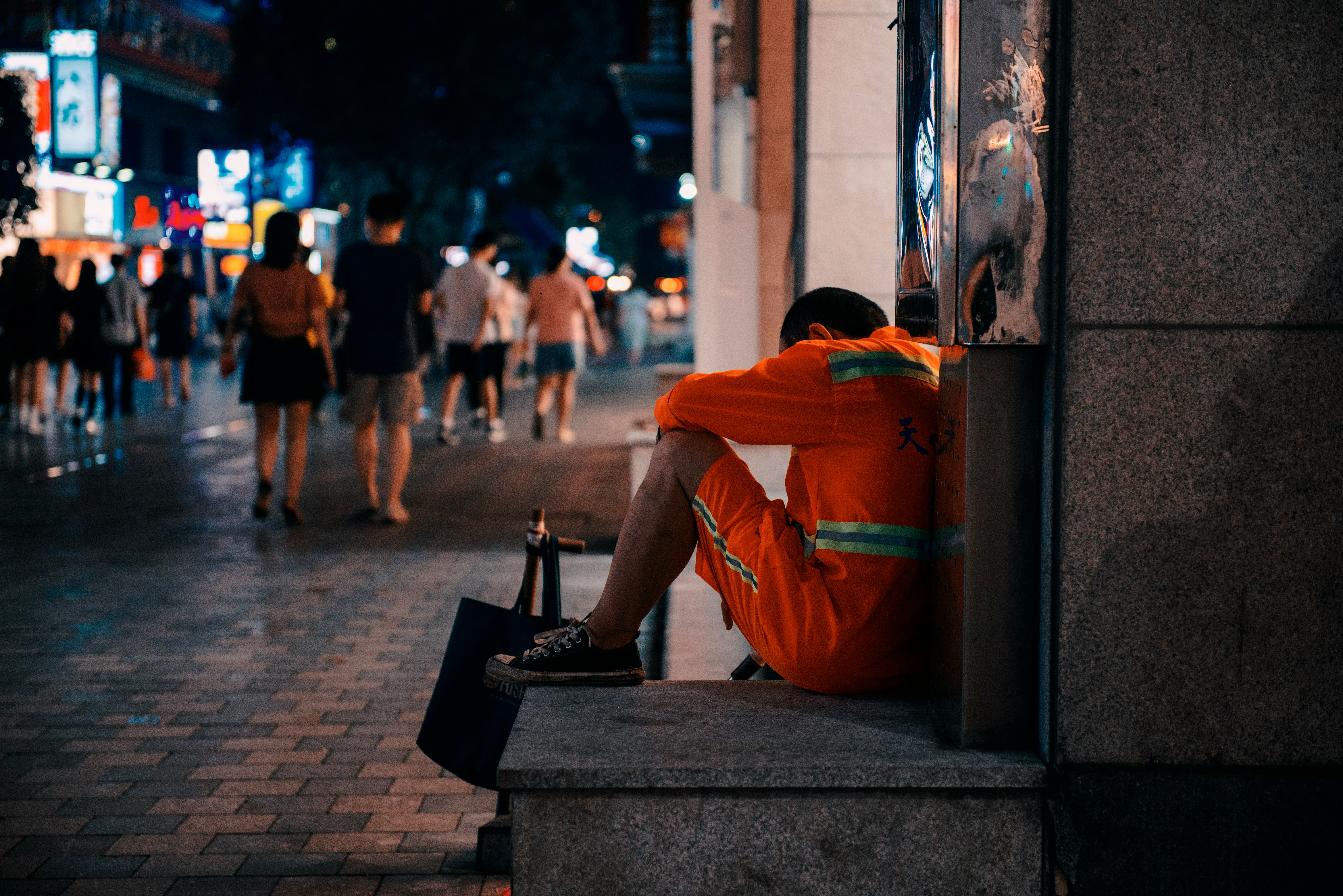 man in orange hoodie sitting on concrete bench